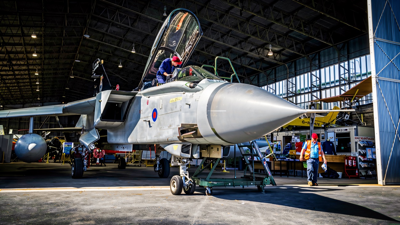 A Tornado jet with its canopy raised while work goes on in the hangar