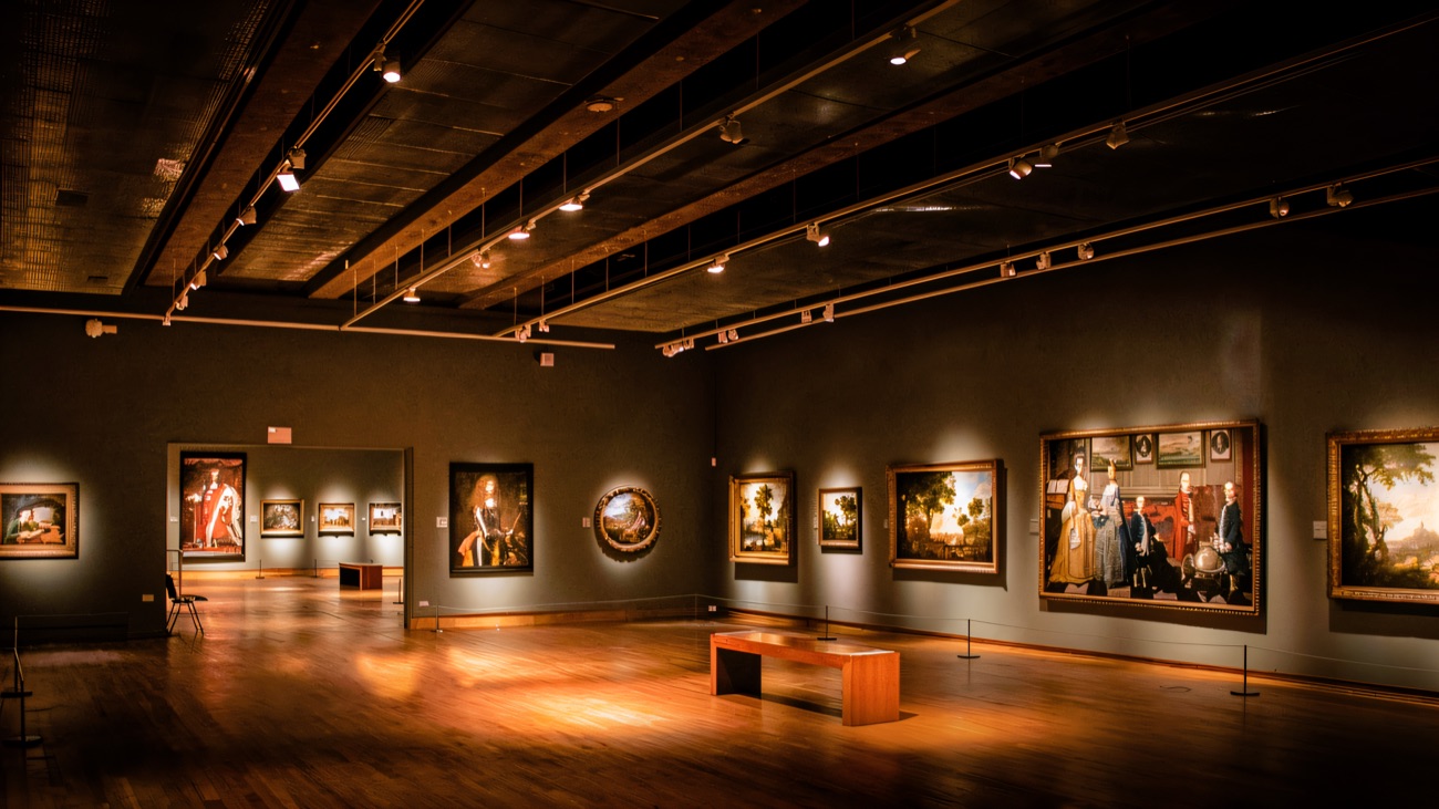 A grand art gallery lined with framed paintings under warm lighting