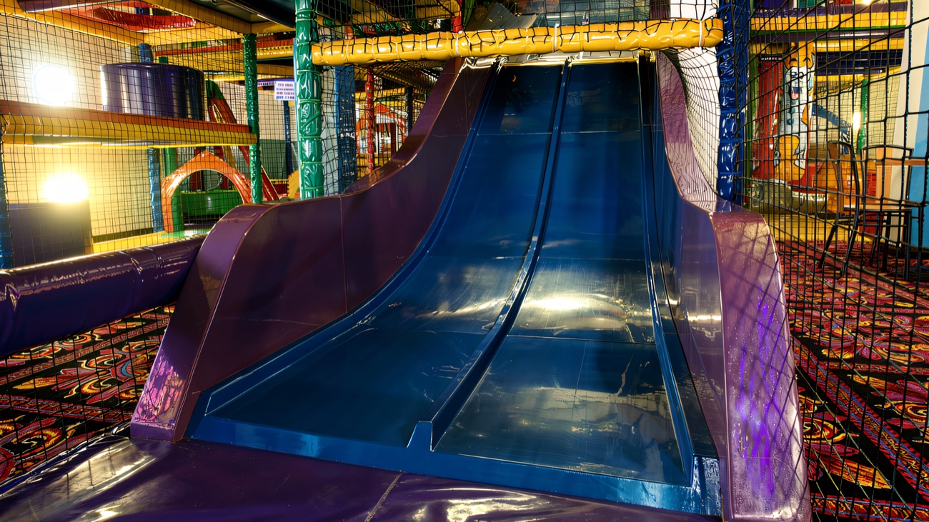 A wide blue double slide dropping onto the padded landing mat