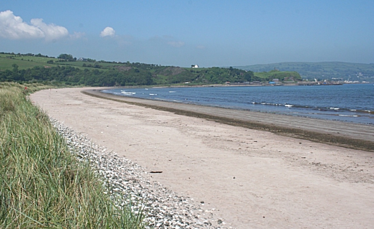The long curved sweep of Waterfoot beach with marram-grass dunes, the sea and the Glens of Antrim in the distance under a blue summer sky