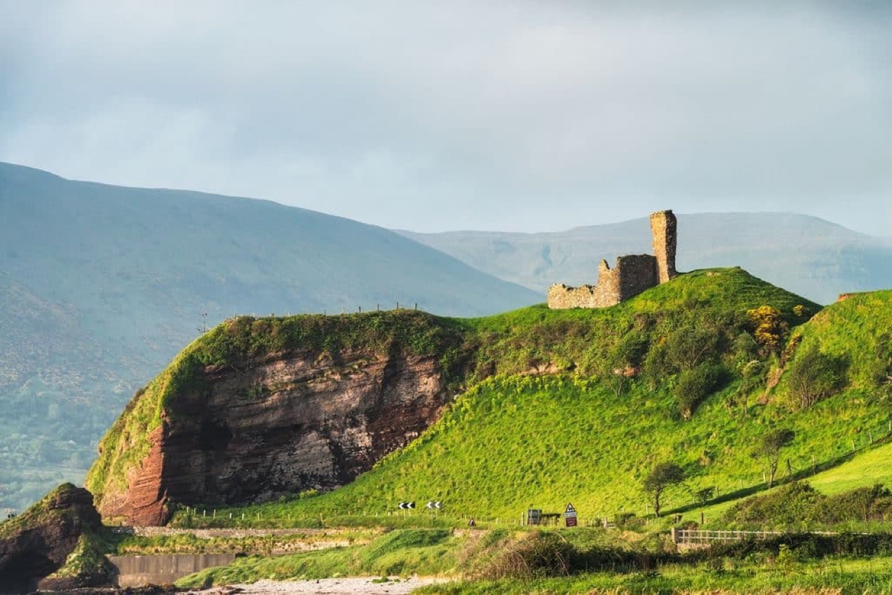 The ruins of Red Bay Castle standing on red-sandstone cliffs above Waterfoot, with the green Glens of Antrim behind