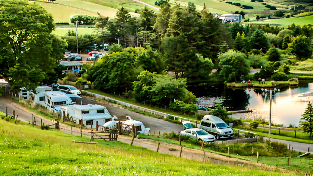 Caravans and campervans pitched beside the lake with people out in a rowing boat and green hills rising behind