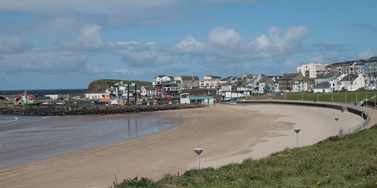 The curve of West Strand beach at low tide with the harbour, promenade and Portrush town behind