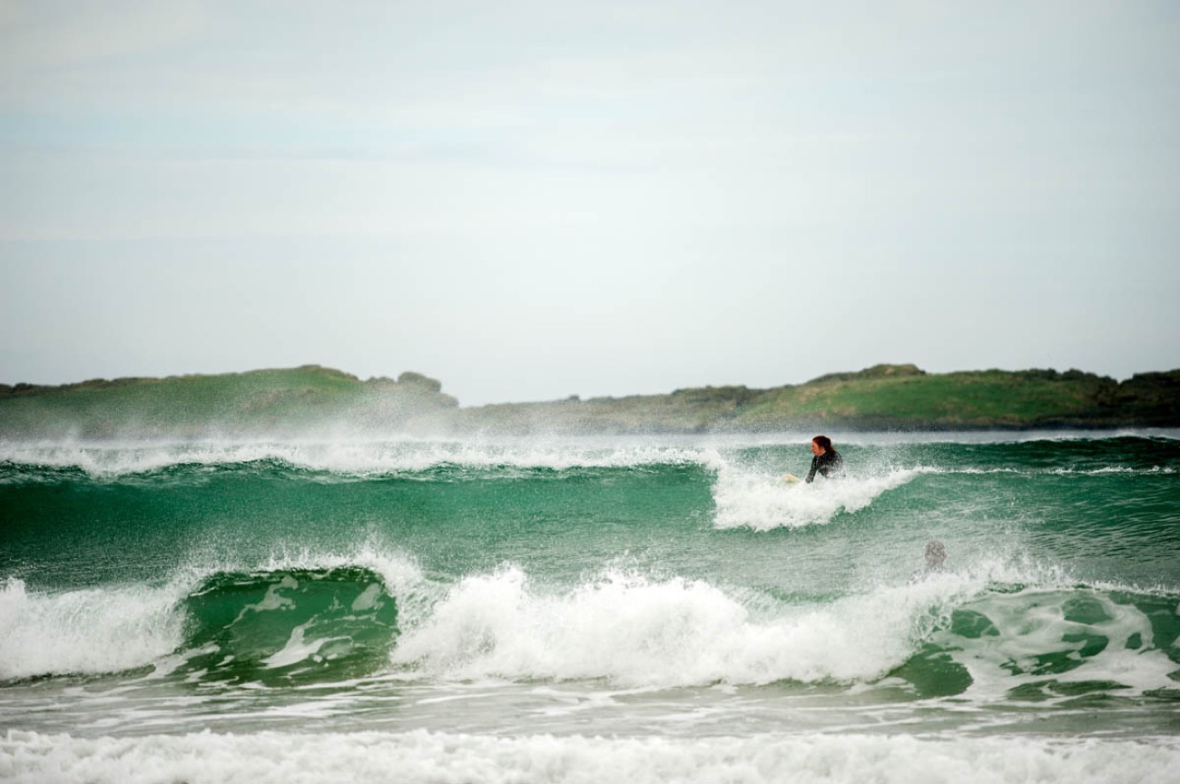 A surfer riding a green wave in the surf at Whiterocks Beach, Portrush